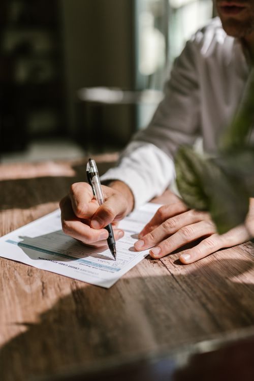 A person writing on a business document with a pen on a wooden desk
