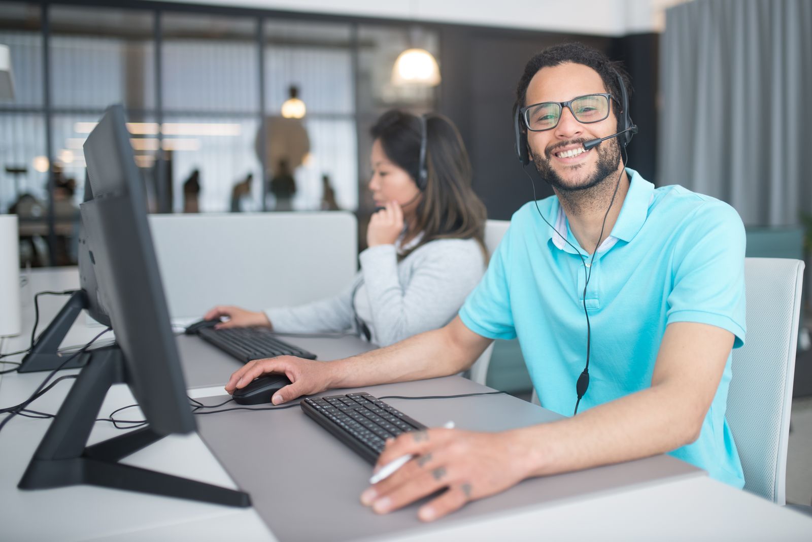 Two customer support agents wearing headsets and answering questions at their computers
